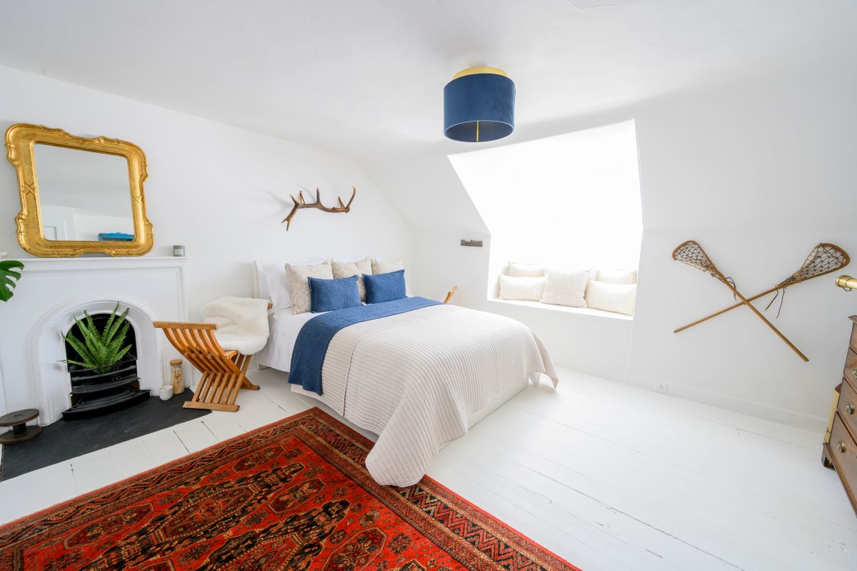 white farmhouse bedroom with large red rug, blue cushions and antique mirror; Kirsty Anderson photographs 'Blawlowan', a Georgian townhouse in Bridge of Allan featuring on series eight of Scotland's Home of the Year ie SHOTY