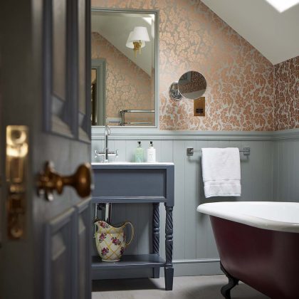 bathroom with blue cabinet, floral wallpaper and red roll-tip bath