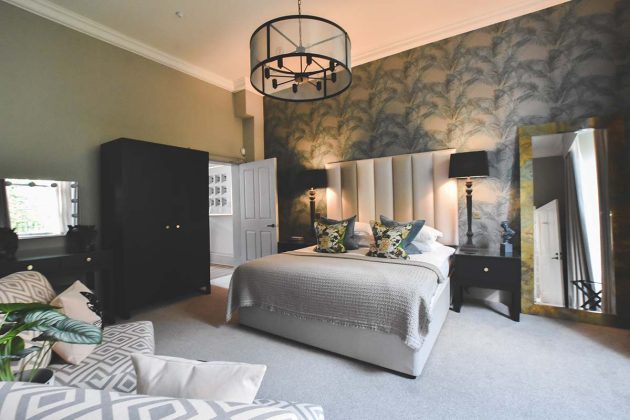 velour headboard on a silver bed with patterned green wallpaper and statement light fittings