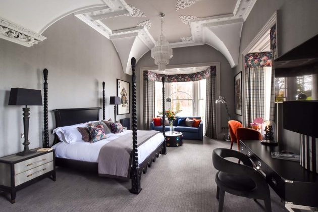 black four poster bed with white cornicing and black sofas beside bay windows in a hotel