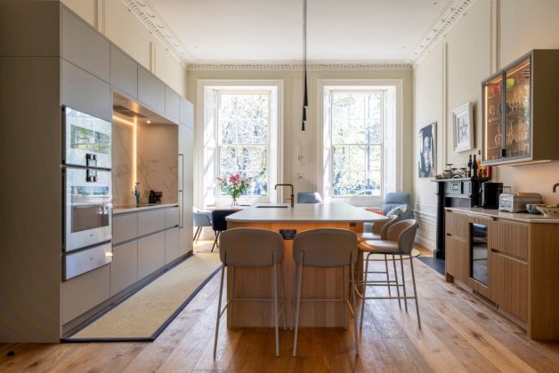 big kitchen with wooden breakfast bar, grey modern bar stools, herringbone wooden flooring, grey cabinetry and a backlit splashback