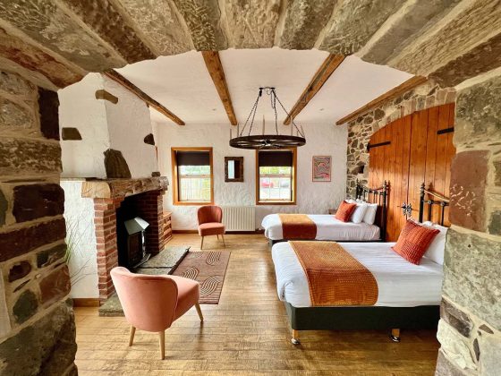 white hotel bed with ornage linens and wooden beams with a stone roof in the oak tree in on loch lomond, one of Scotland's best luxury hotels, cottages