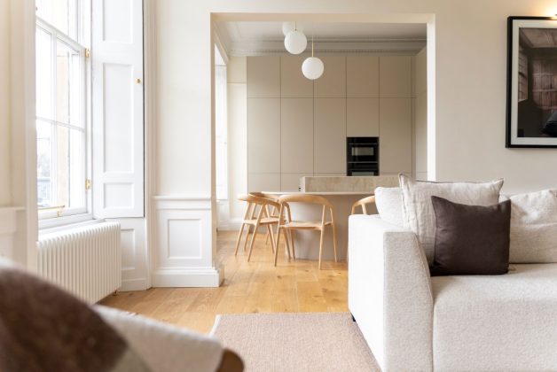 living room with white sofa, wooden floors, oak dining table and chairs, and white wall panelling with spherical pendant lights