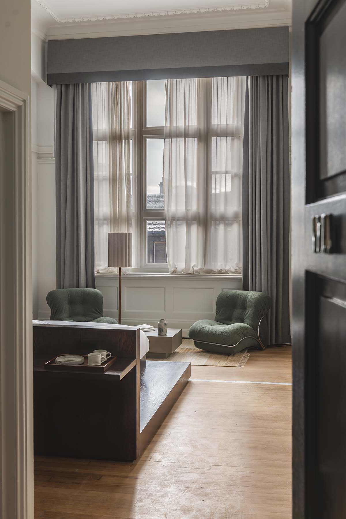 arthouse glasgow room with soft oak flooring, grey curtains and shallow bed with green boucle armchair