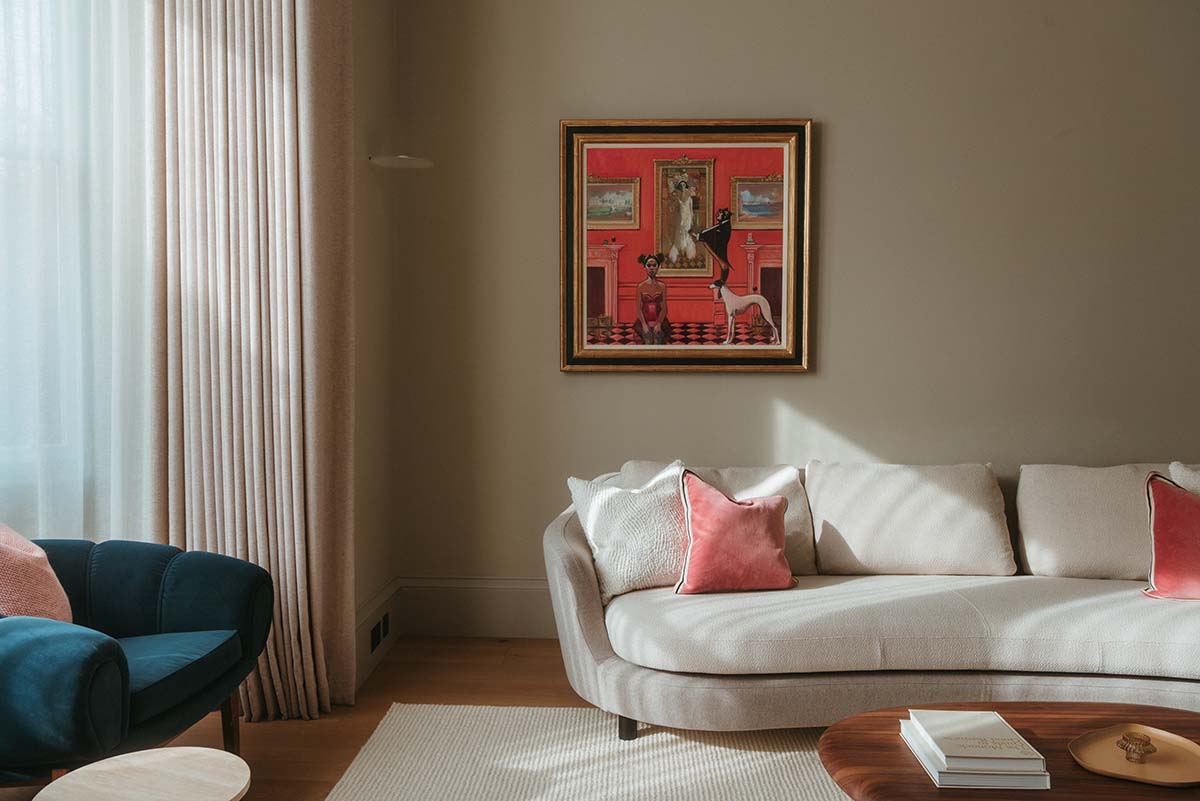 a sleek but colourful living room with white sofa and pink cushions by studio september and bann